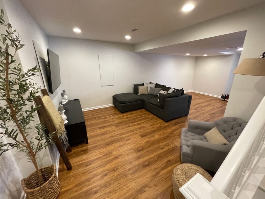 Finish basement contractors creating a clean, modern living space with recessed lighting, hardwood floors, and a comfortable sectional seating area