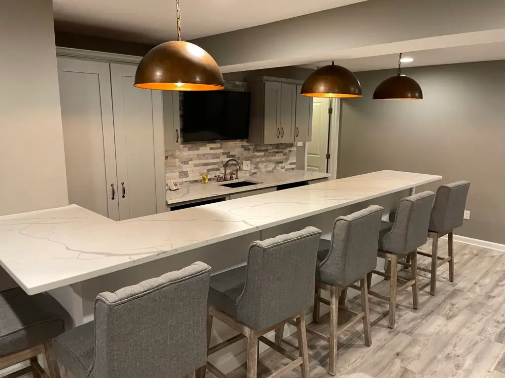 Pittsburgh basement finishing project featuring a bright, modern open-concept design with a large quartz island, bar seating, pendant lighting, and a comfortable lounge area with sectional sofa and mounted TV.