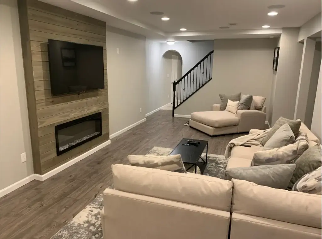 Basement remodelers Pittsburgh homeowners trust build cozy lounge spaces with reclaimed wood accent walls, electric fireplaces, and plush cream sectional seating like this one, designed by Pittsburgh Basement Finishing.